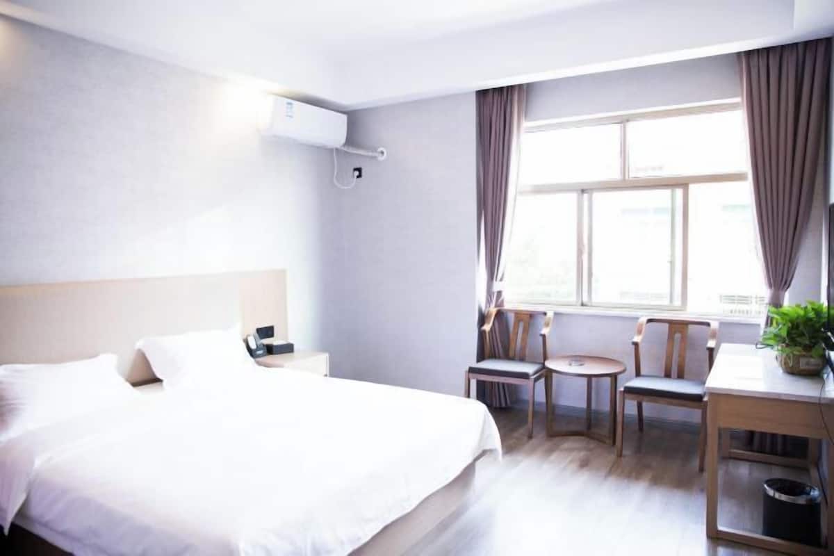 A hotel room with a bed, bedside table, lamp, and a window with curtains.