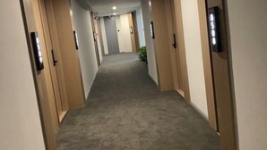 A hotel hallway with carpeted floors, wooden doors, and a light-colored wall.