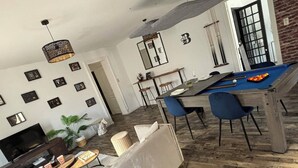 Un amplio salón con mesa de billar, un sofá y una televisión.
