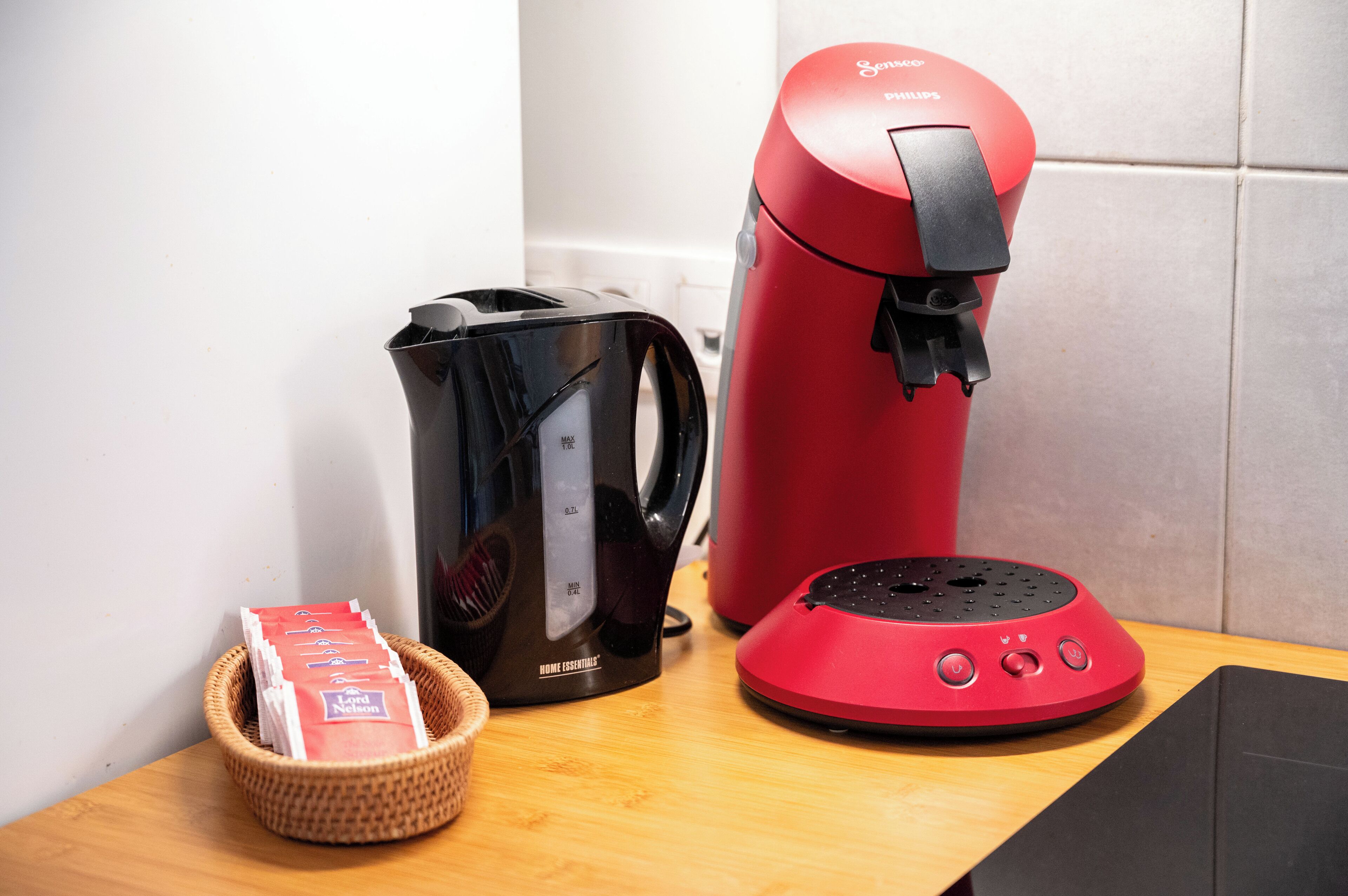 A kitchen with a coffee maker, a kettle, and a basket of coffee pods.