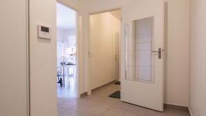 A hallway with a tiled floor, a door with a frosted glass panel, and a thermostat on the wall.