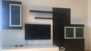 Ein modernes Wohnzimmer mit einem an der Wand befestigten Flachbildfernseher, einer weißen Unterhaltungseinrichtung darunter und einem schwarzen Schrank mit Glastüren.