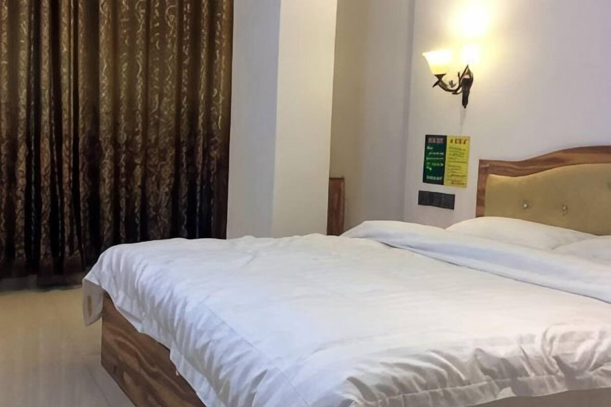 Une chambre d’hôtel avec un lit, des rideaux, un luminaire fixé au mur et un panneau sur le mur.