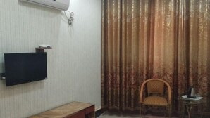 Une chambre d’hôtel avec un lit, un téléviseur fixé au mur, une petite table avec une bouilloire et une chaise.