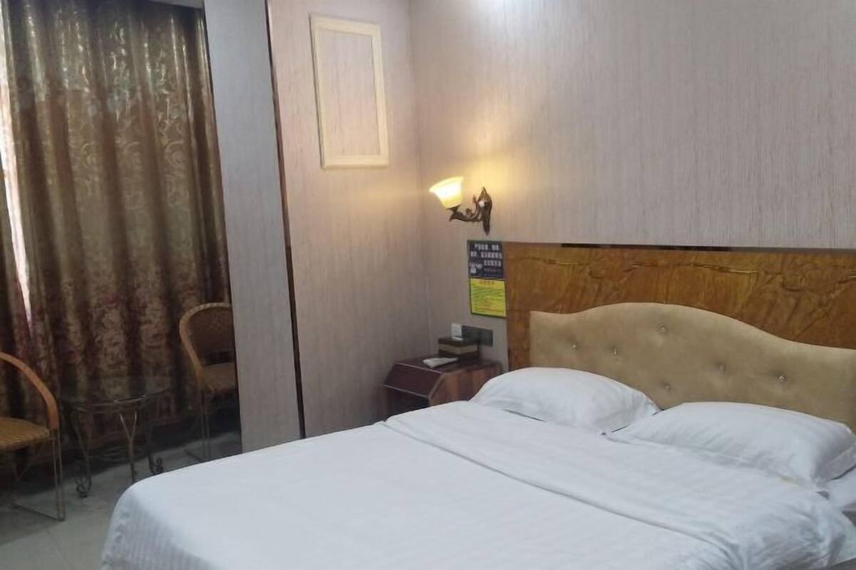 Une chambre d’hôtel avec un lit, une table de chevet, une lampe, une chaise et un rideau.