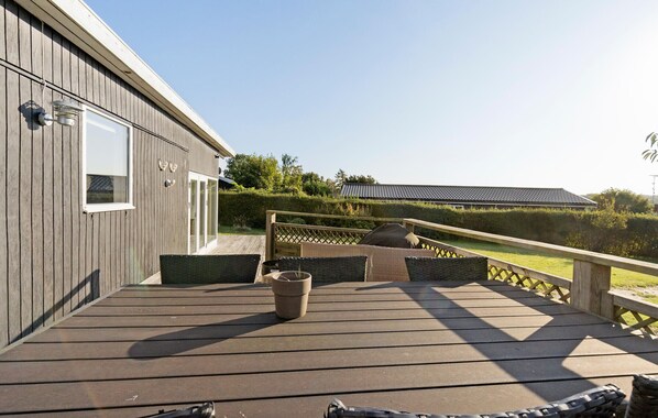 A wooden deck with outdoor seating, a potted plant, and a view of a building with a tiled roof. - Stunning home in Roskilde (Roskilde)