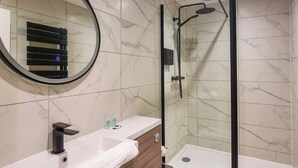 Ein modernes Badezimmer mit Marmorboden, einem runden Spiegel, einem weißen Waschbecken, einer hölzernen Waschtischbank, einer Toilette und einer Duschkabine.