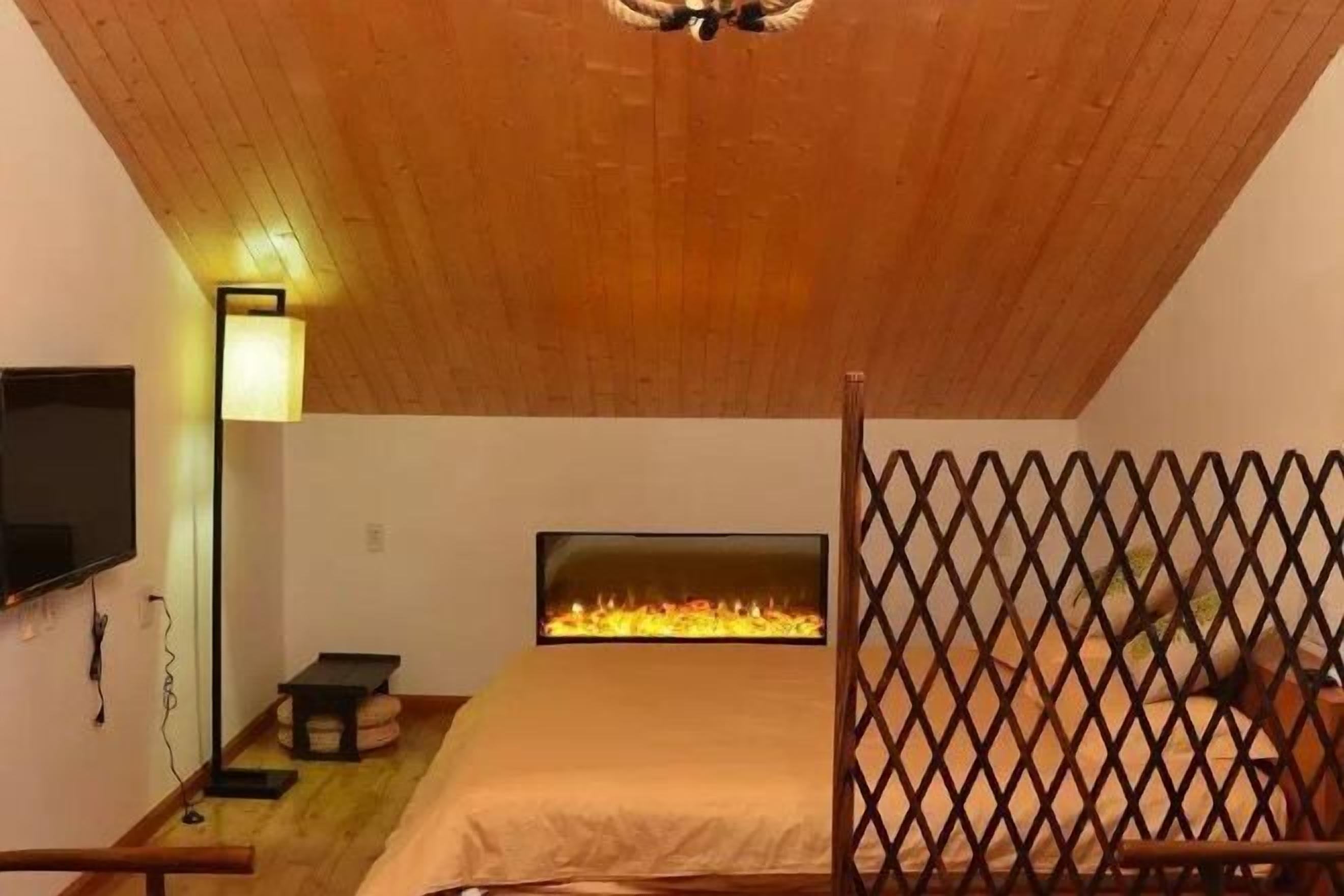 Un dormitorio con techo inclinado, un televisor fijado a la pared, una mesita de noche, una cama con cabecero y una chimenea.