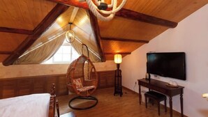 A cozy attic room with a sloped ceiling, a hanging chair, a desk, and a TV.