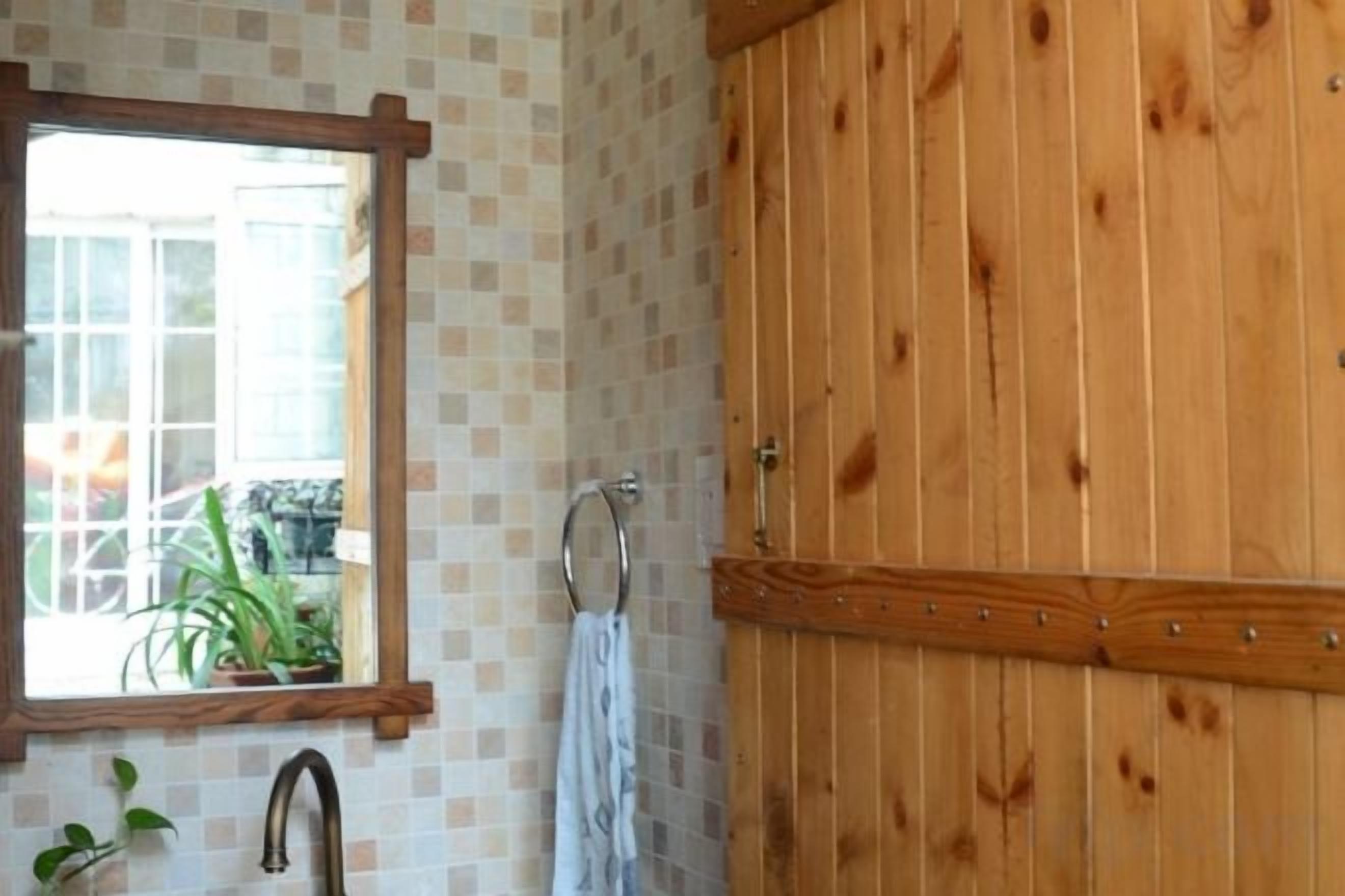 A bathroom with a wooden door, a mirror, and a window with a view of the outside.