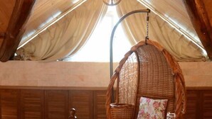 A rustic interior with a hanging chair, wooden paneling, and a large window with draped fabric.