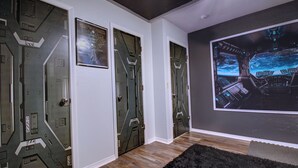 Un couloir avec trois portes au design futuriste, un grand écran mural affichant une scène spatiale et un plancher en bois.