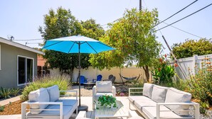 Une terrasse avec des meubles blancs, un parasol bleu et un hamac.