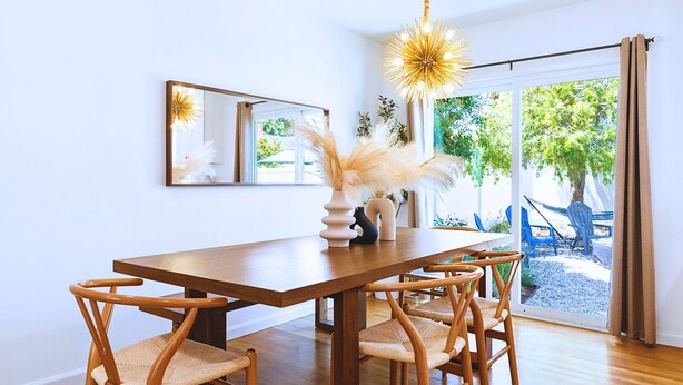 Un coin repas avec une table et des chaises en bois, un vase contenant des objets décoratifs et un grand miroir au mur.