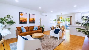 Un salon moderne avec un canapé en cuir marron, des fauteuils blancs, une table basse en bois et un coin repas comprenant une table et des chaises.