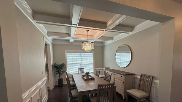 A dining room with a long wooden table, chairs, a chandelier, a potted plant, and a large mirror on the wall.
