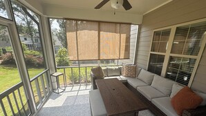 A covered patio with a wooden table, a cushioned bench, and a sofa.