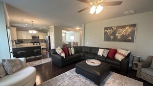 A modern living room with a sectional sofa, ottoman, and a large rug. There is a kitchen in the background with a bar area.