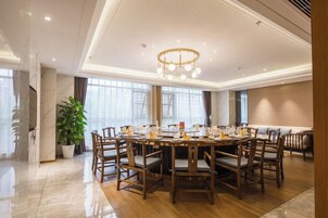 Un comedor amplio con una mesa redonda y sillas, una araña y ventanas grandes.