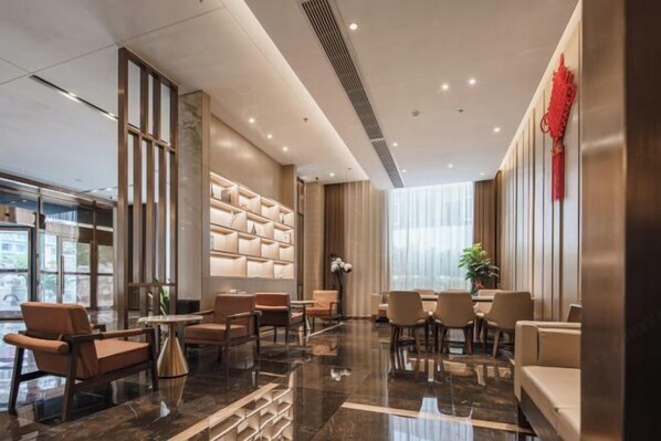 A modern hotel lobby with a seating area, a decorative wall, and a large window. - Wellton City Hotel (Ganzhou Railway Station) (Ganzhou)