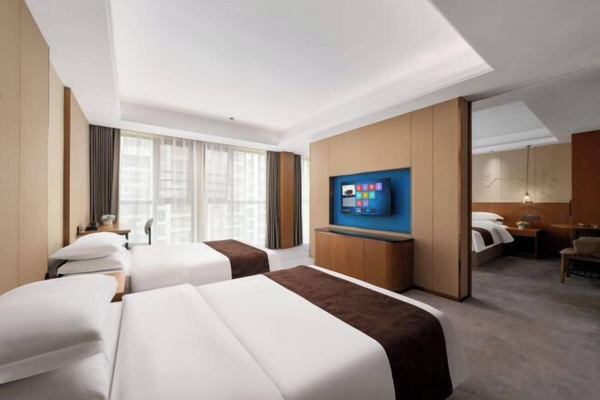 Een hotelkamer met twee bedden, een televisie, een bureau en een groot raam.