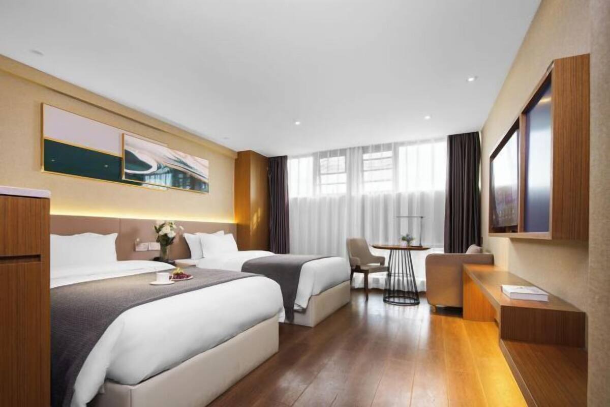 Hotelkamer met twee bedden, een bureau, een stoel, een televisie en een raam met gordijnen.