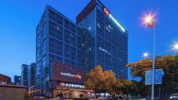 A modern hotel building with a prominent 'Wellton City' sign, multiple floors, and a well-lit facade.