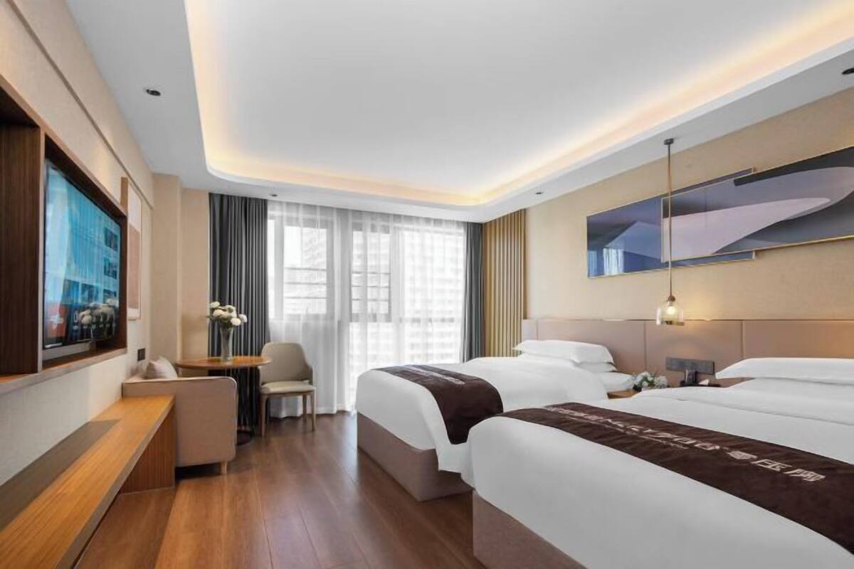 Een hotelkamer met een groot bed, een bureau, een stoel, een televisie en een raam met gordijnen.