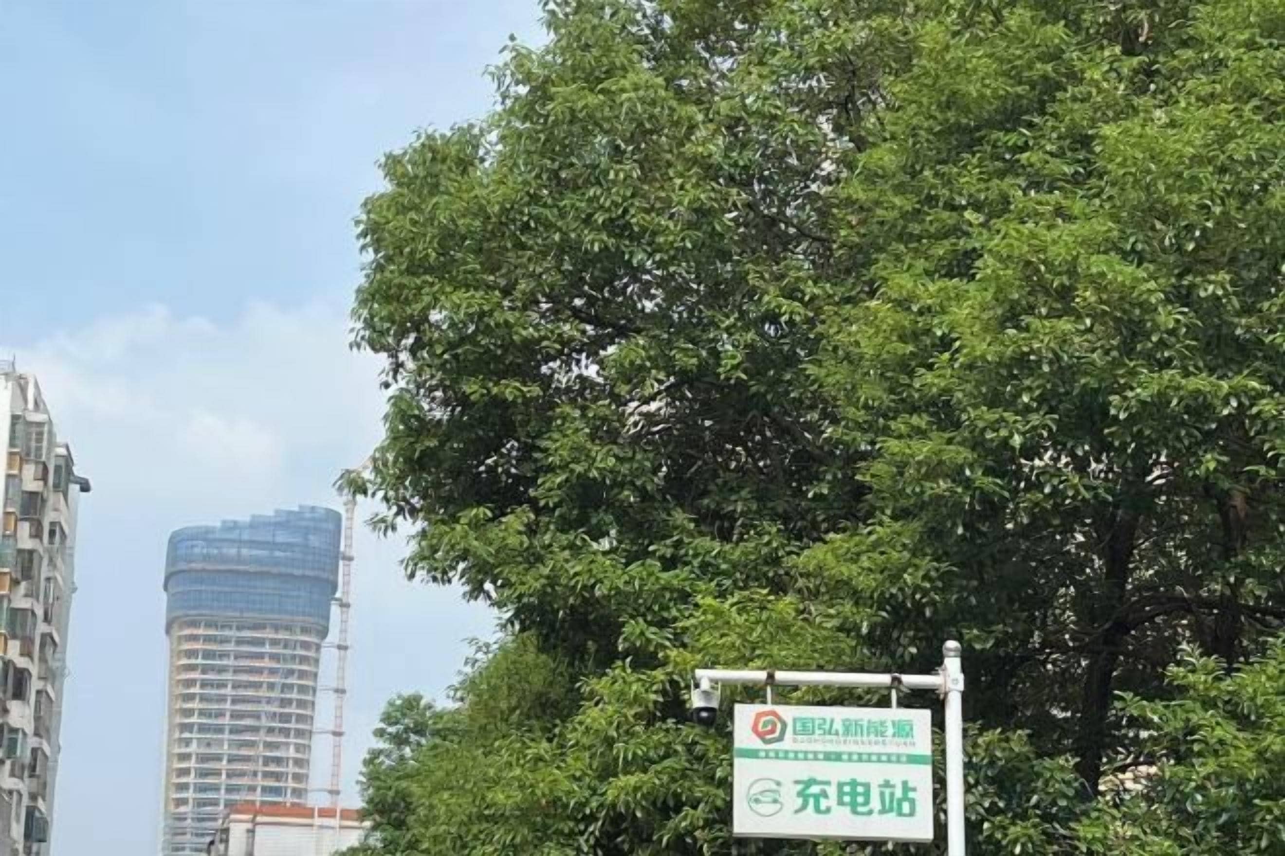 Ein Schild mit Text, ein Baum und ein Gebäude im Hintergrund.