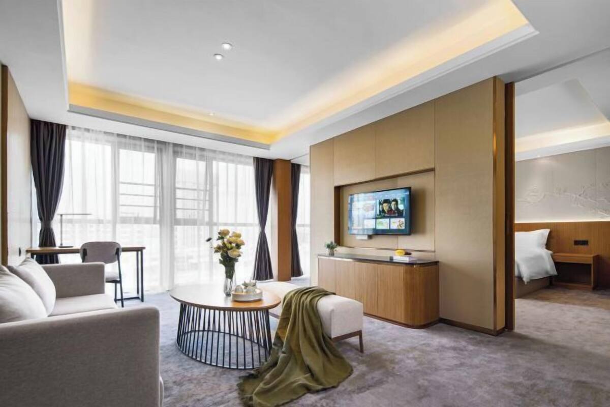 Een moderne hotelkamer met een ronde eettafel, een bank, een aan de muur bevestigde televisie en een bed met hoofdeinde.