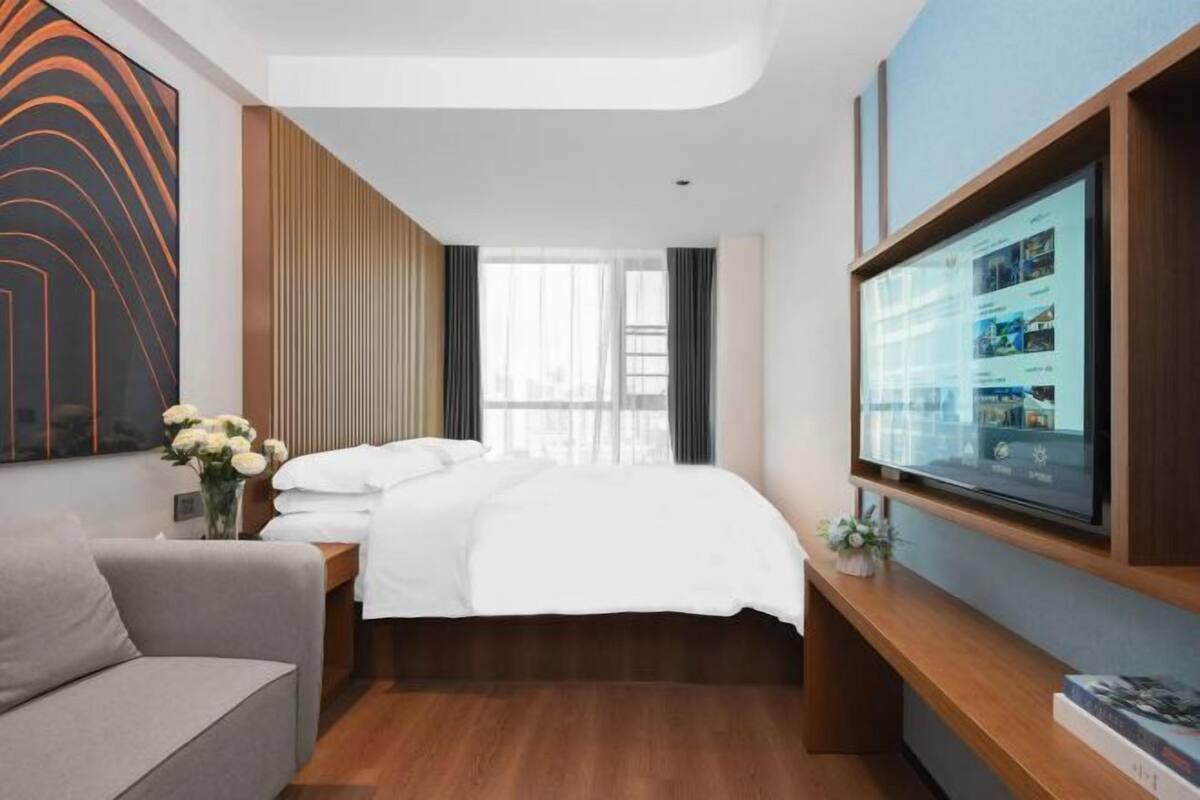 Een hotelkamer met een bed, een televisie, een bank en een aan de muur bevestigde televisie.
