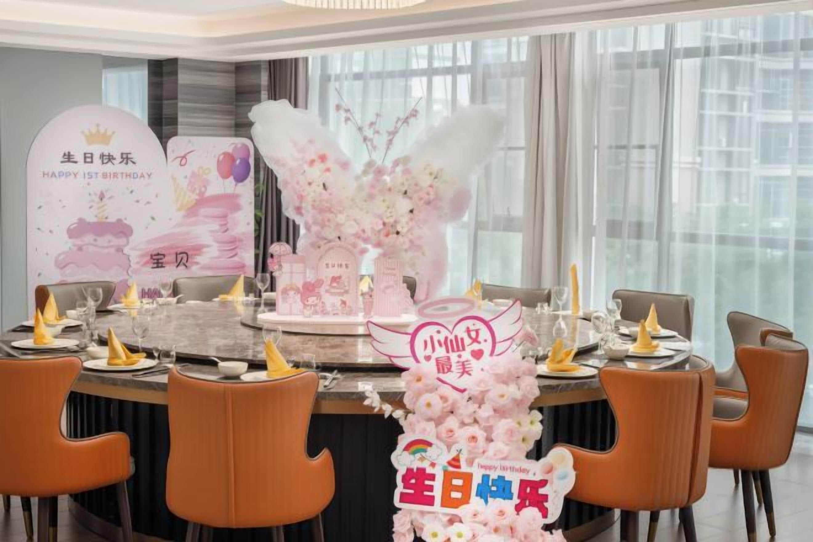 A dining area with a round table set for a birthday celebration, featuring a cake and floral decorations.