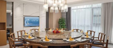 A round dining table with chairs, a chandelier, and a screen in the background.