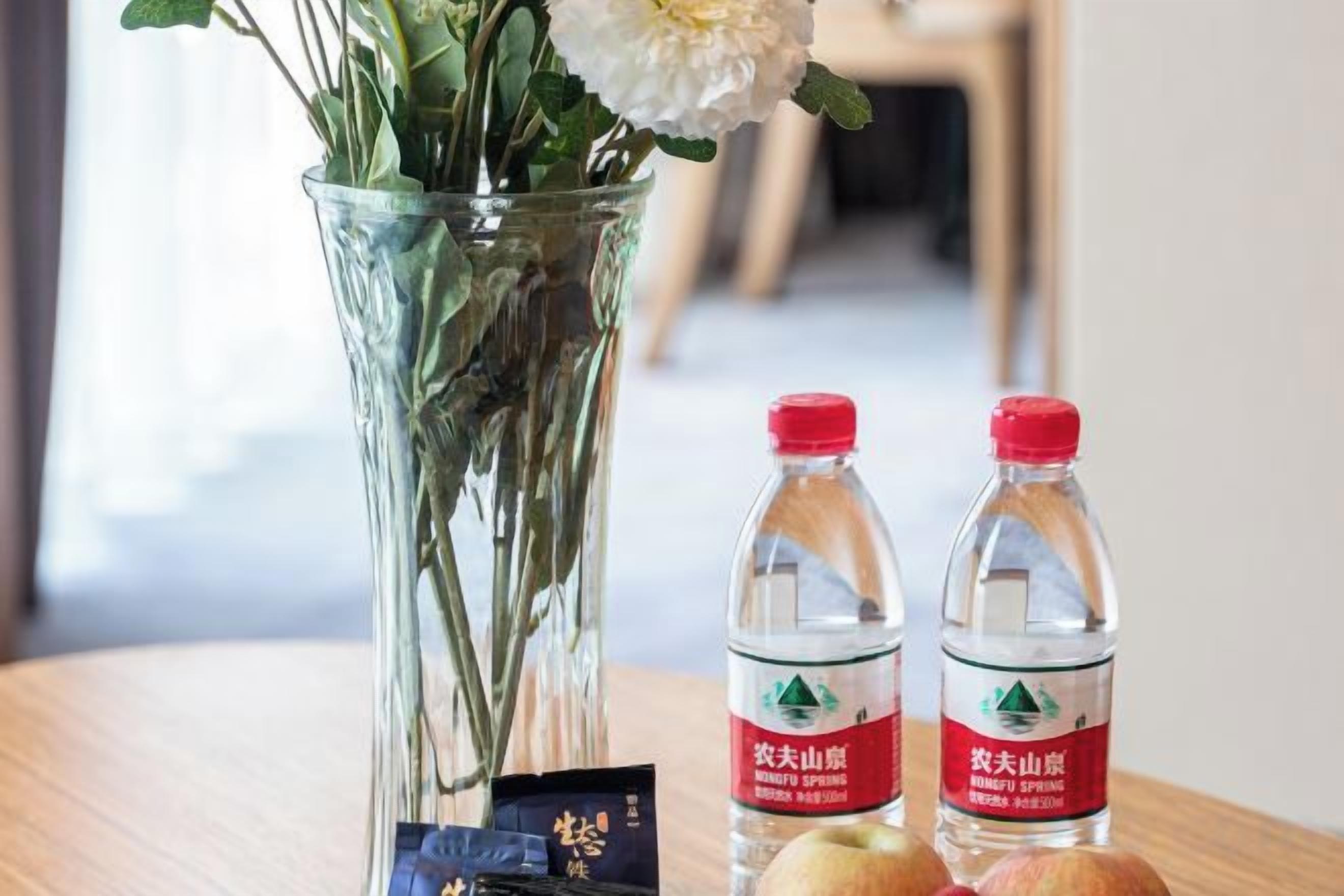 Un florero de vidrio transparente con flores y dos botellas de agua con etiquetas sobre una superficie de madera.