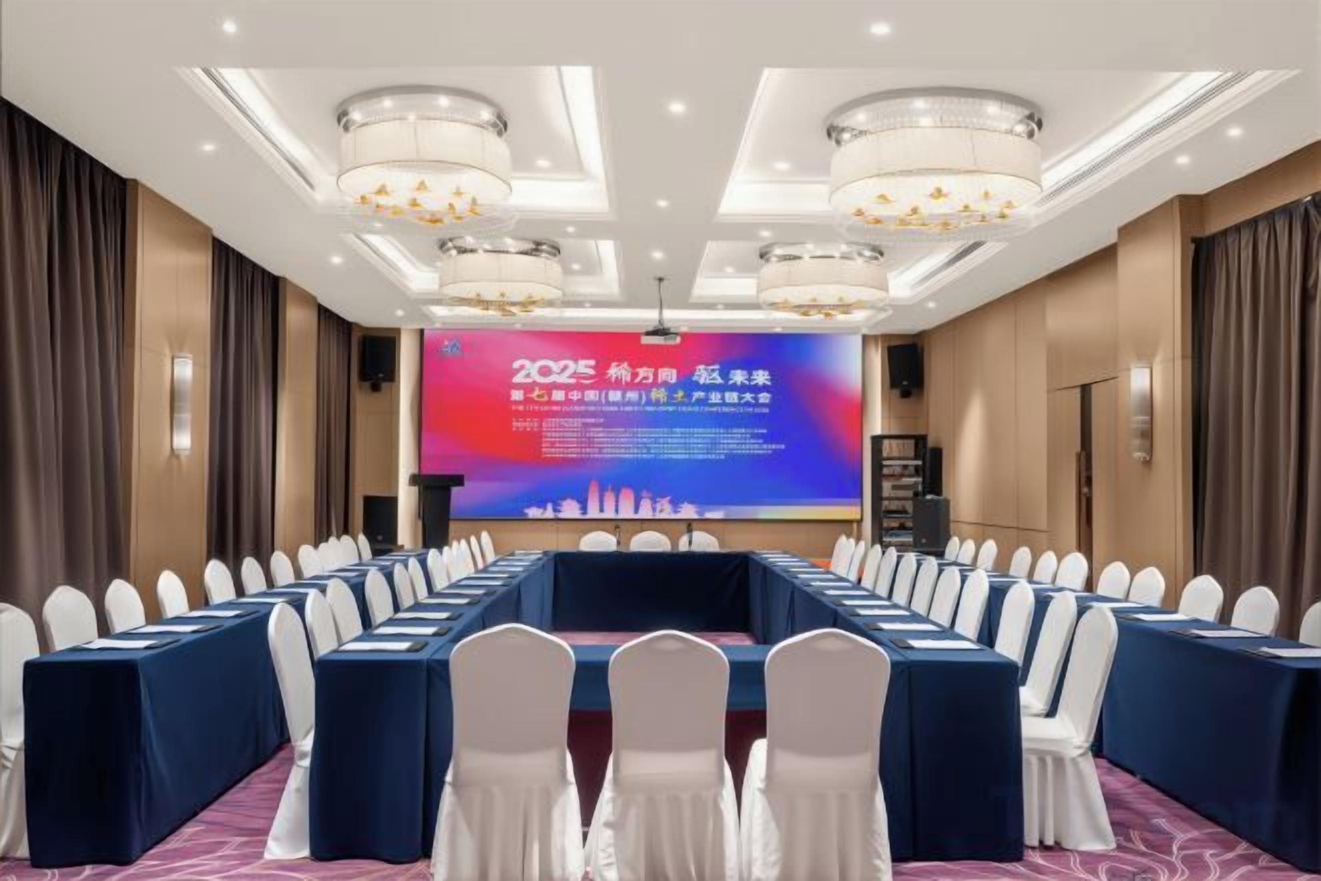 A conference room with a long table, rows of chairs, a large screen, and a chandelier.