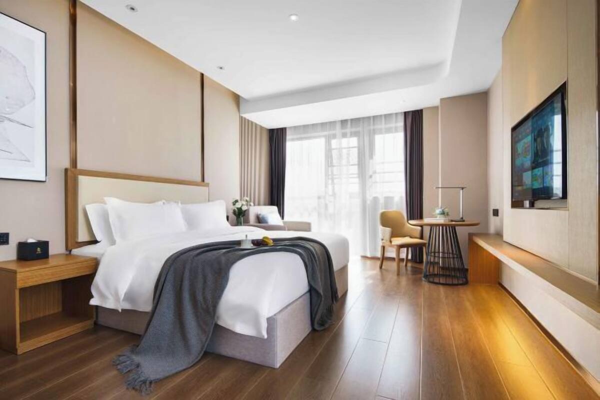 Een moderne hotelkamer met een groot bed, nachtkastje, een klein tafeltje met lamp en een aan de muur bevestigde televisie.