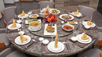 Une table ronde dressée pour un repas, avec différents plats, des verres et des serviettes.