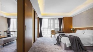 A hotel room with a bed, a seating area, a small table, and large windows.