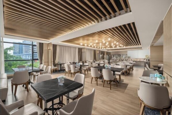 Un comedor moderno con varias mesas y sillas, ventanas amplias y un diseño contemporáneo en el techo.