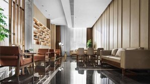 A modern hotel lobby with a glass coffee table, leather sofas, and a built-in shelving unit.