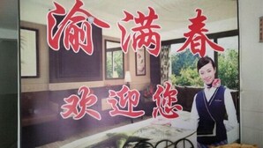 A room with a bed, a nightstand, and a window. There is a poster with Chinese characters and a person standing next to it.