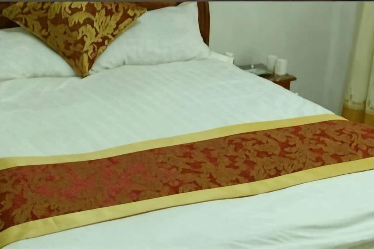 Un lit avec une literie blanche et une couvre-lit aux motifs rouges et dorés.