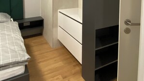 Un dormitorio con cama, cabecera verde, cómoda blanca y armario con espejo.