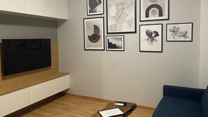 Una sala de estar con un televisor de pantalla plana, una mesa de centro con un control remoto y un sofá azul.