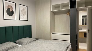 Un dormitorio moderno con cama, armario y baño visible a través de una puerta abierta.