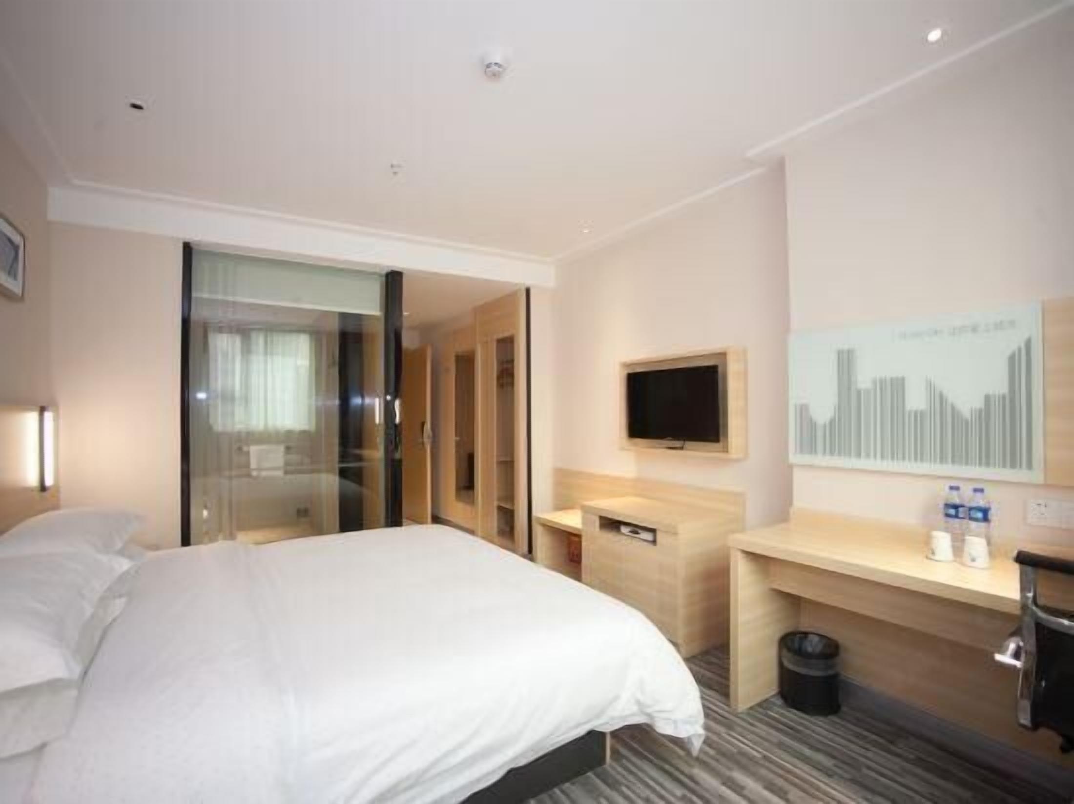 Ein Hotelzimmer mit Bett, Schreibtisch, Fernseher und einem Fenster mit Blick auf die Stadt.