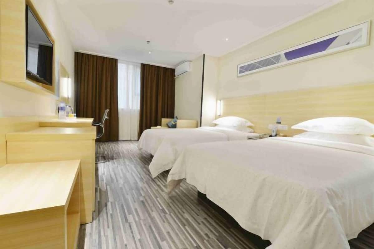 A hotel room with two beds, a wooden desk, a mirror, and a window with curtains.