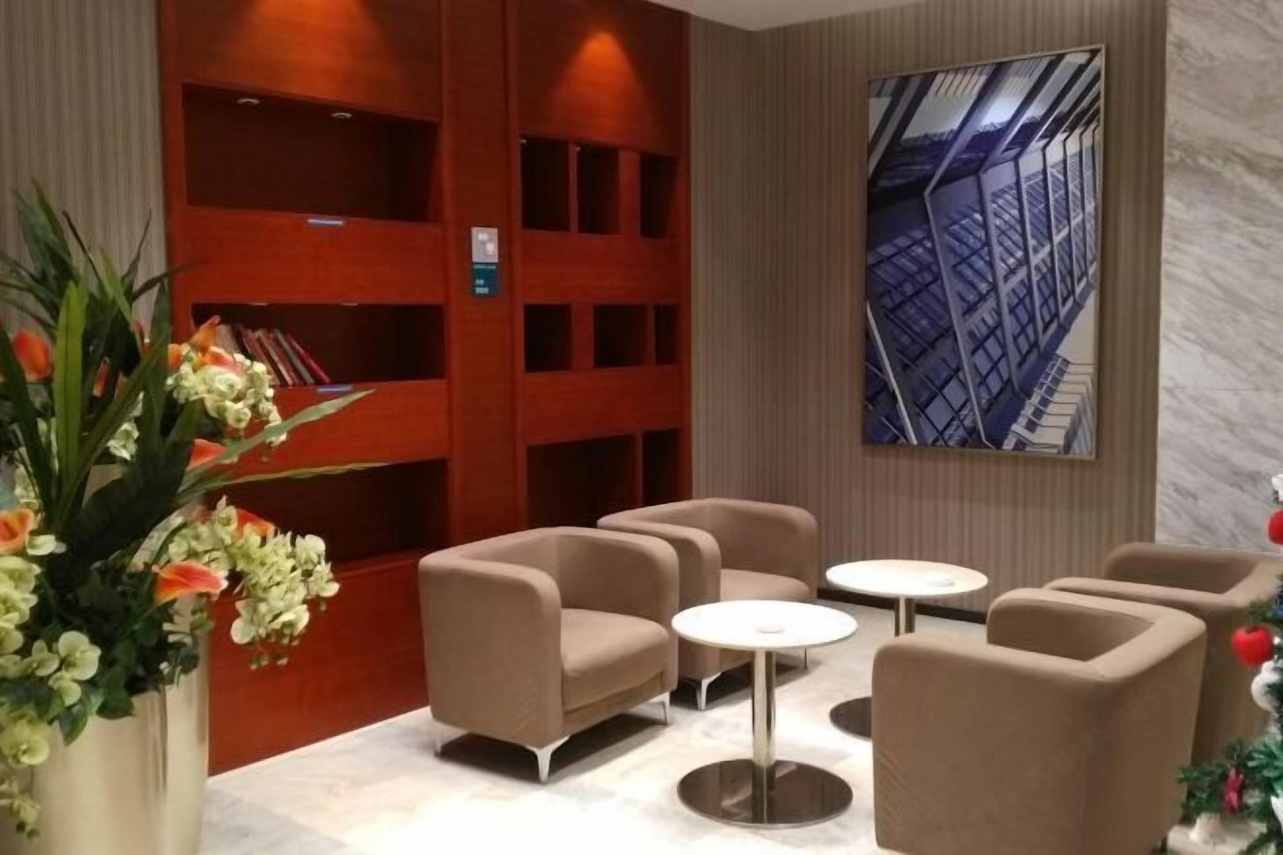 A modern lobby with a wooden reception desk, beige armchairs, and a marble floor.