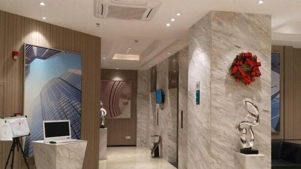 A modern hotel lobby with a marble floor, a reception desk with a laptop, a TV, and a decorative wreath on the wall. - Queen Design Hotel (Qiandeng Lake Resort Guicheng Subway Station Branch) (Foshan)