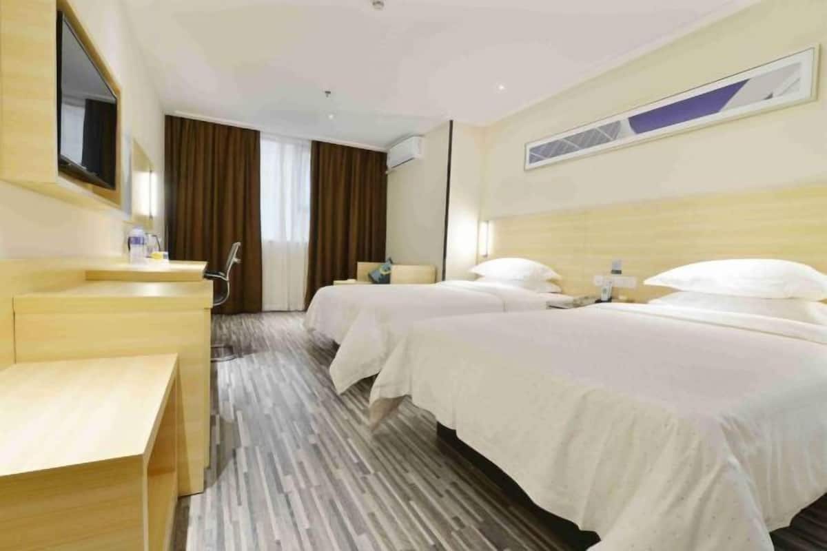 A hotel room with two beds, a desk, a mirror, and a window with curtains.